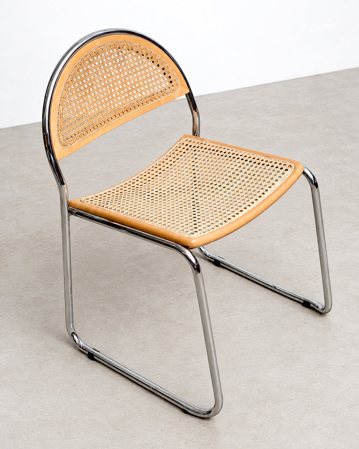 Three-quarter studio view of a single cane chair showing the full chrome frame and caned seat