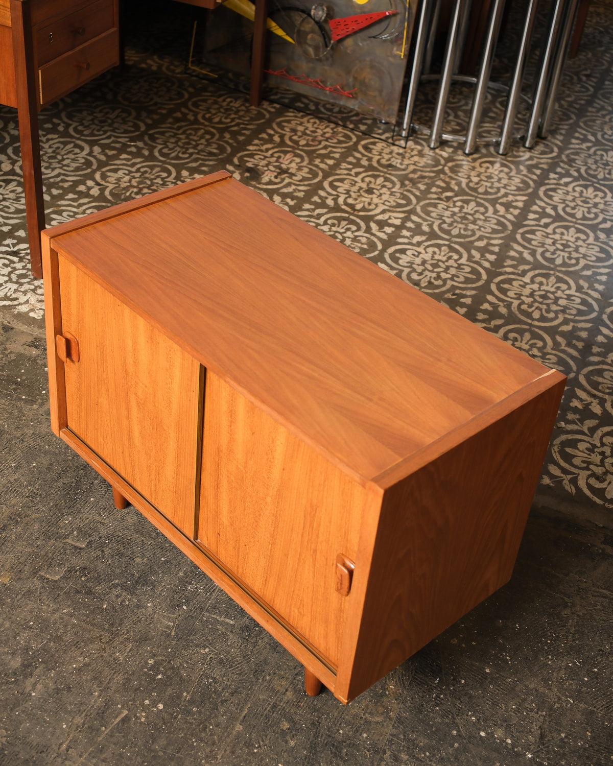 Overhead angled view showing the teak grain on top and the sliding doors with sculpted wood pulls.