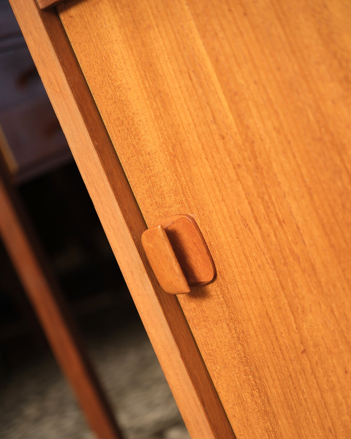 Close-up of the sculpted wood door pull and sliding door seam on the teak cabinet.