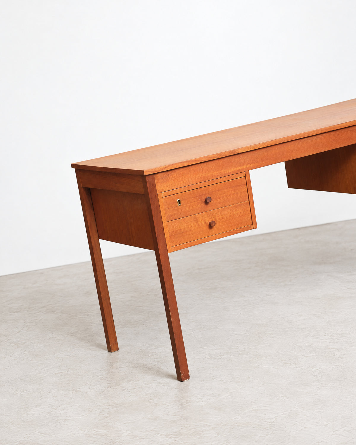 Detail of the desk's tapered leg and drawer front against a plain studio background.