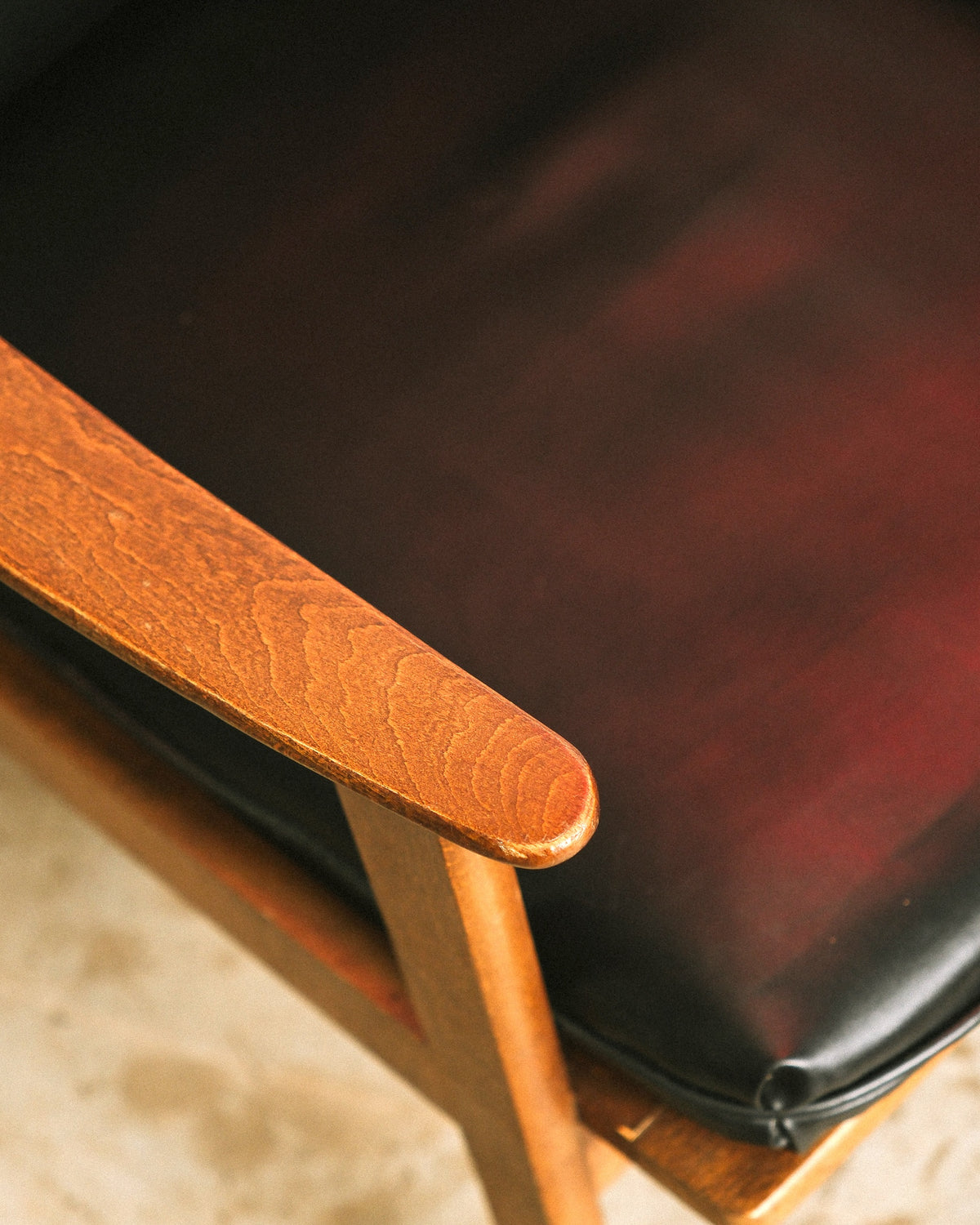 Close-up of the sculpted wood armrest showing natural grain and the black vinyl seat cushion.