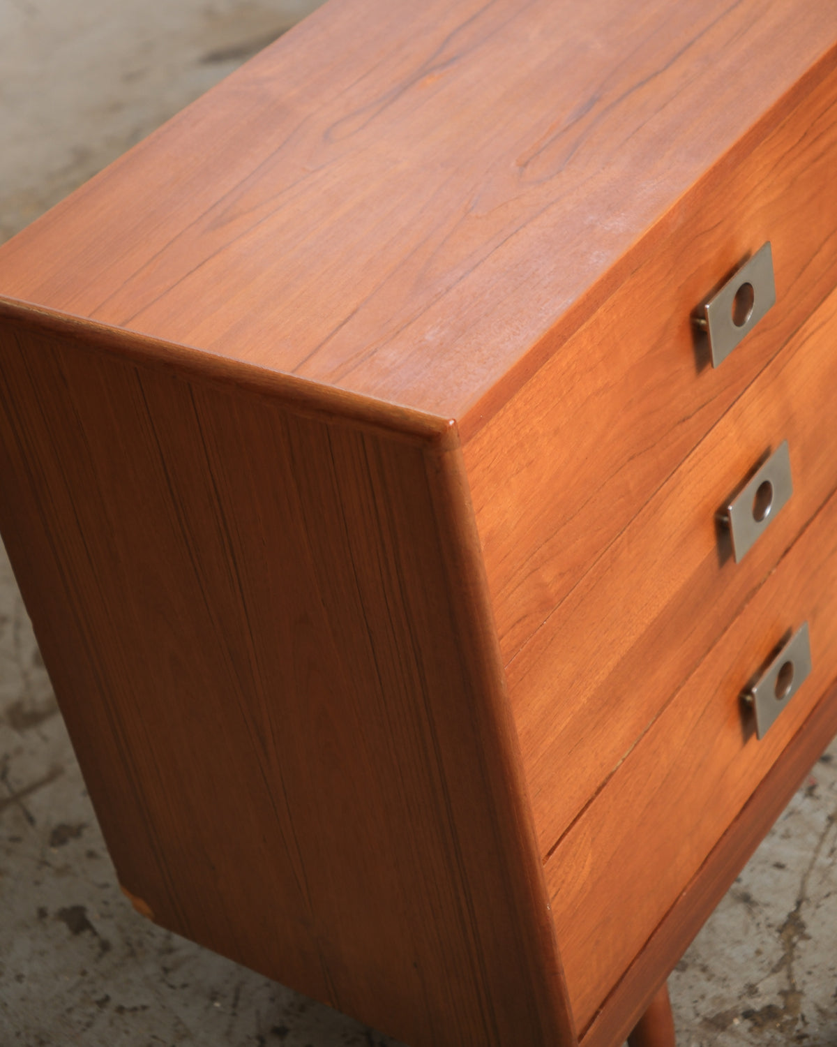 Close-up angled view of the teak dresser's top corner showing grain detail and chrome knob pulls.