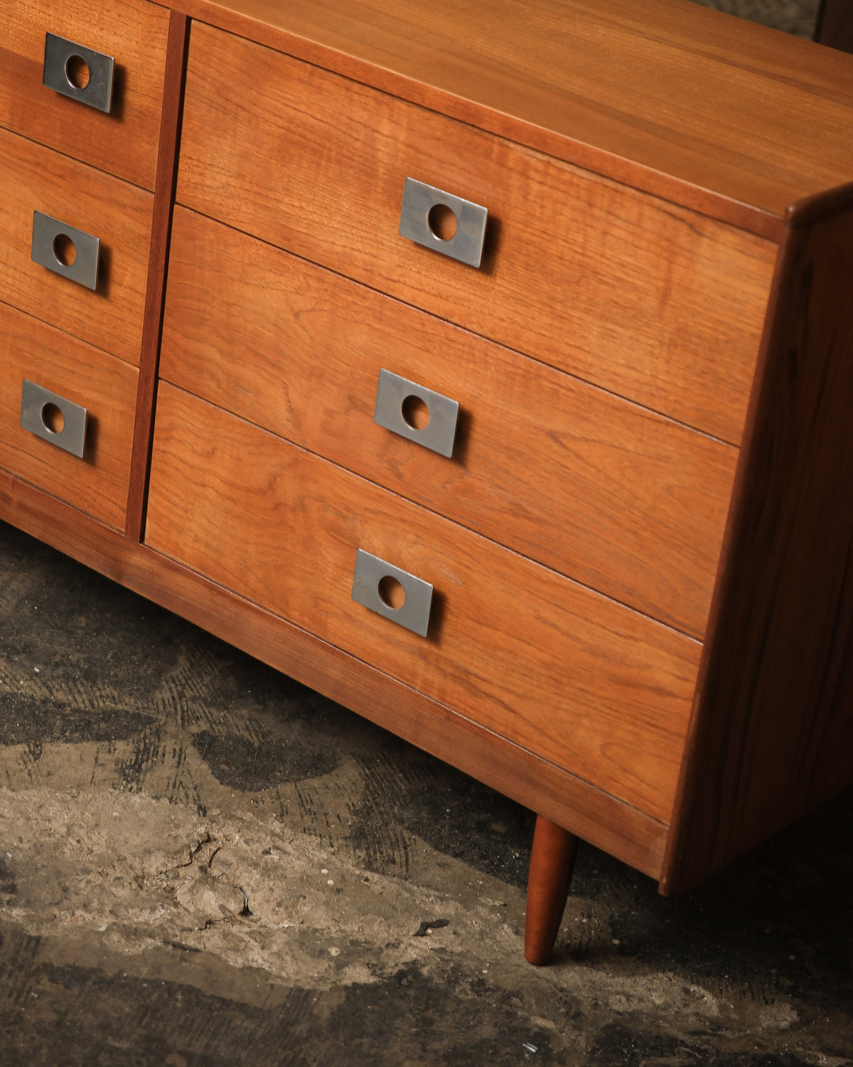 Detail of the drawer fronts, chrome pulls, and tapered leg from a low angle.