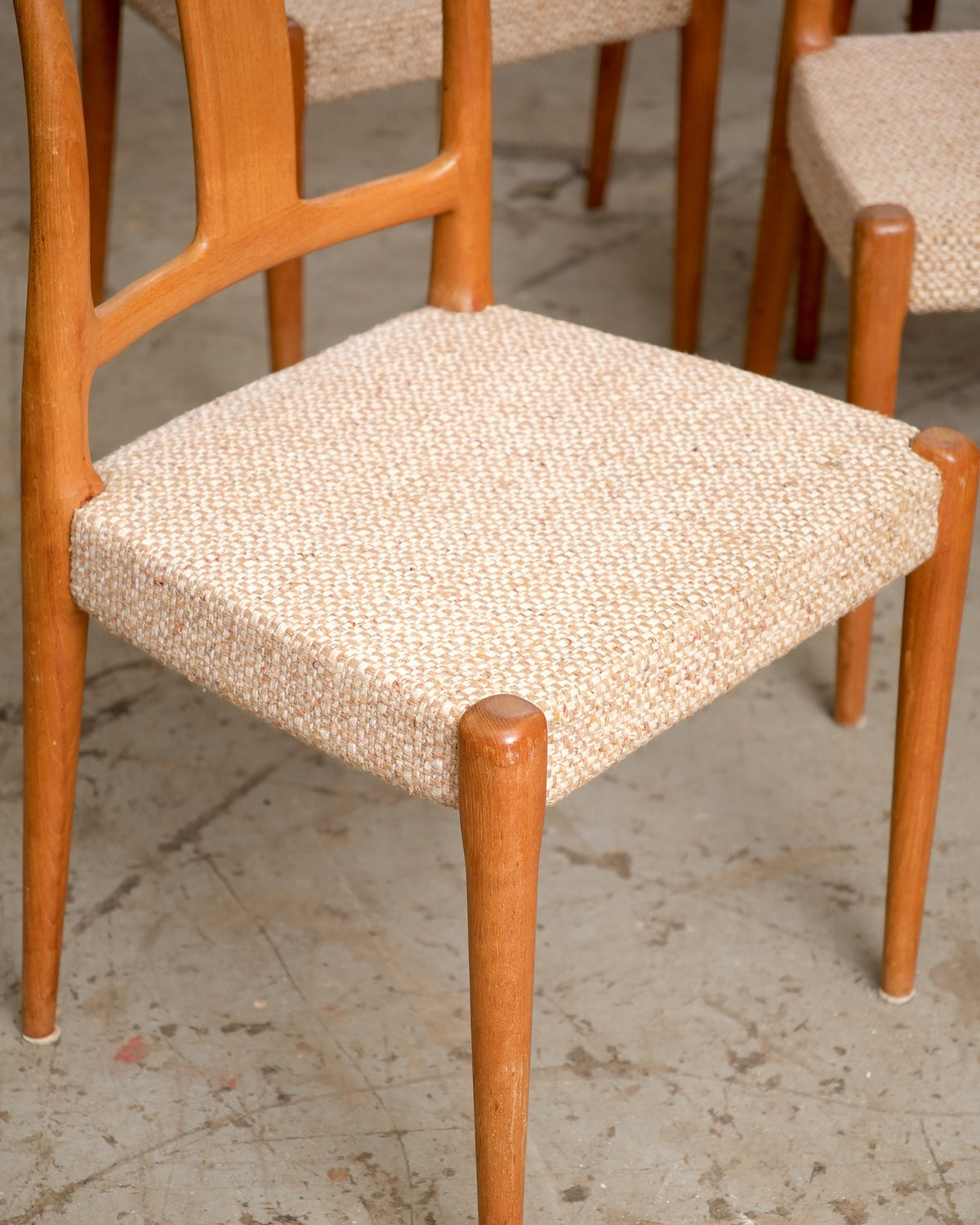 Close-up of a dining chair's tapered teak leg and tweed upholstered seat with other chairs in the background
