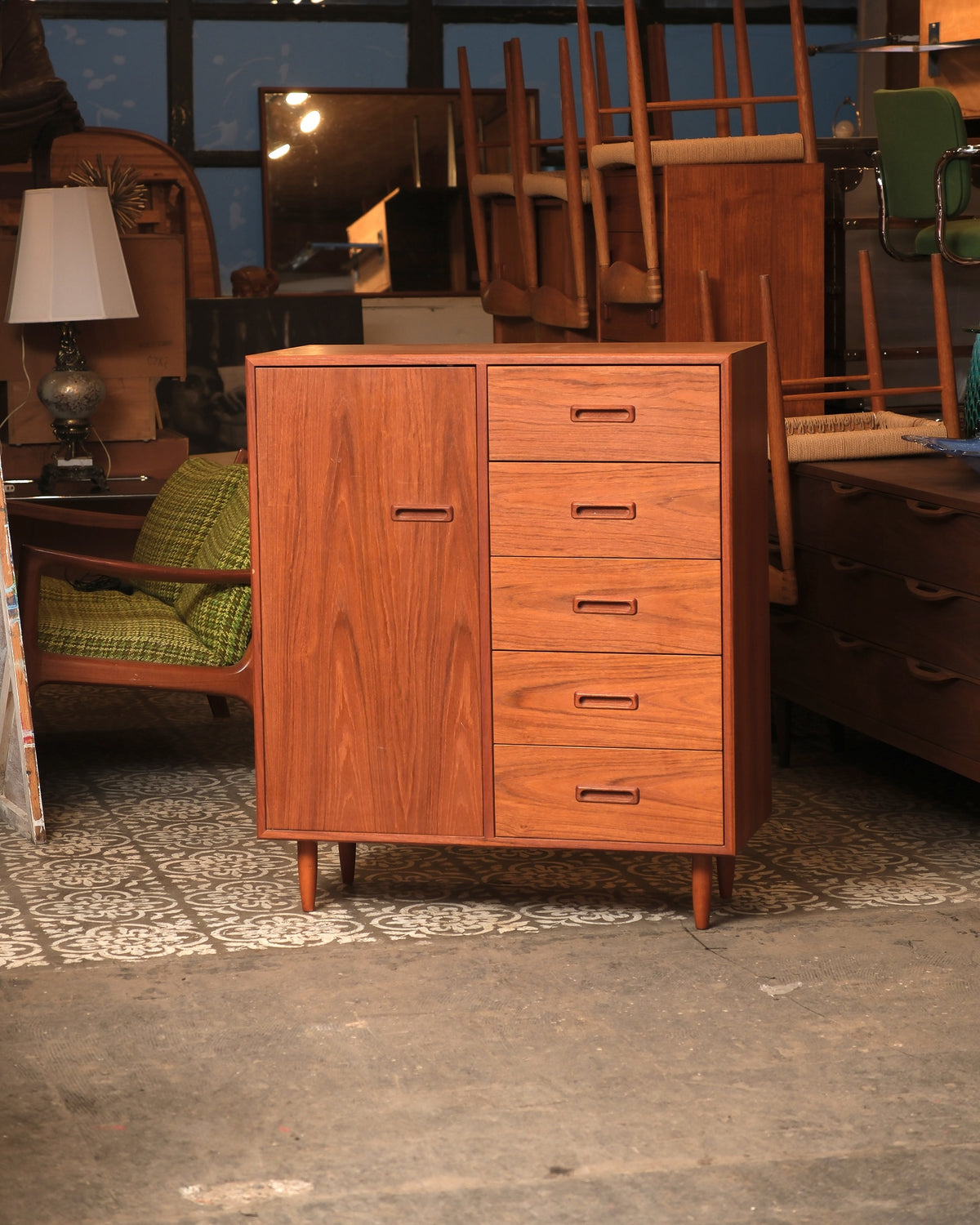 Mid-century modern teak gentleman's chest with door and five drawers, shown in showroom setting.