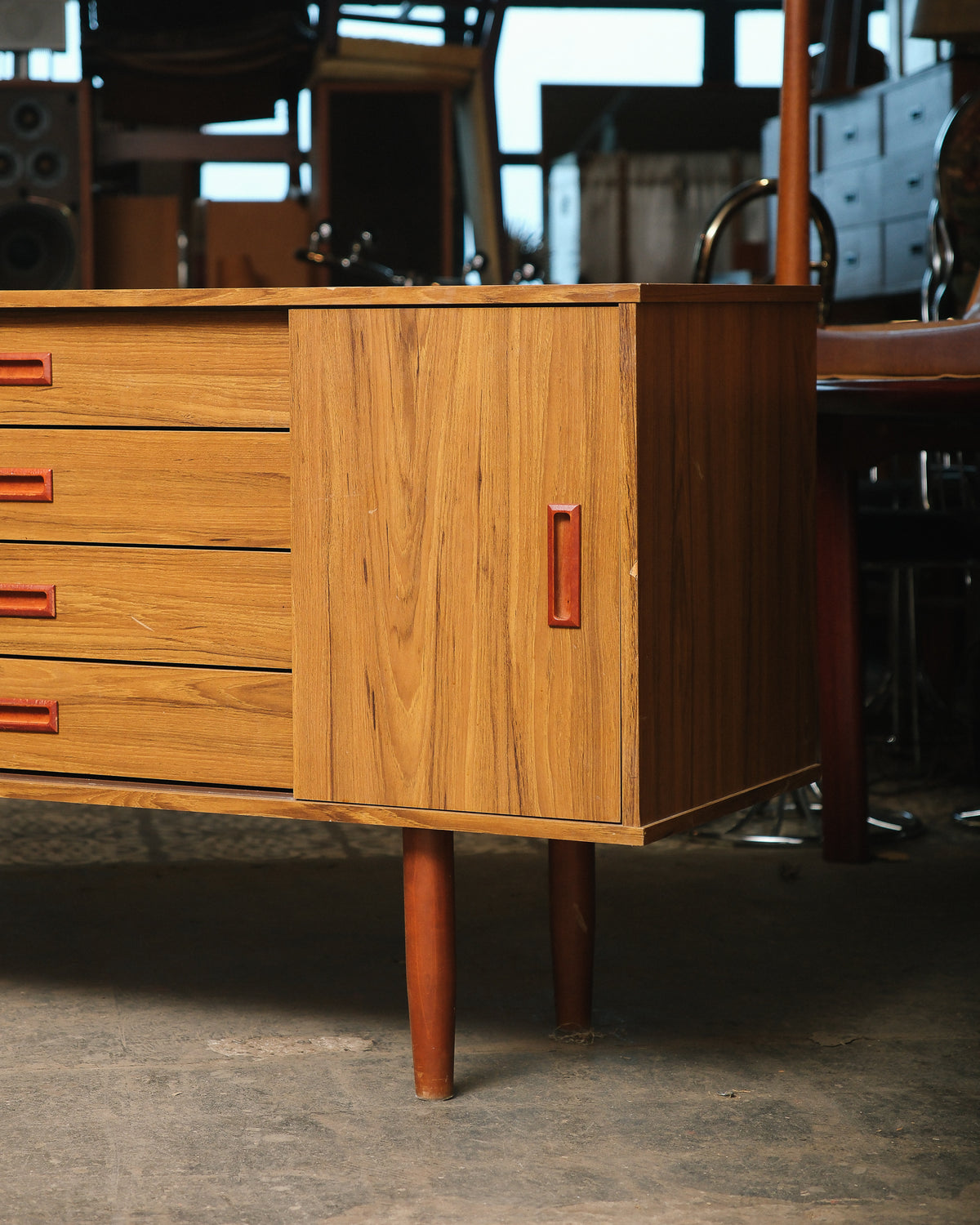 Close-up of the sliding cabinet door and sculpted pull handle, showing teak grain and tapered leg.