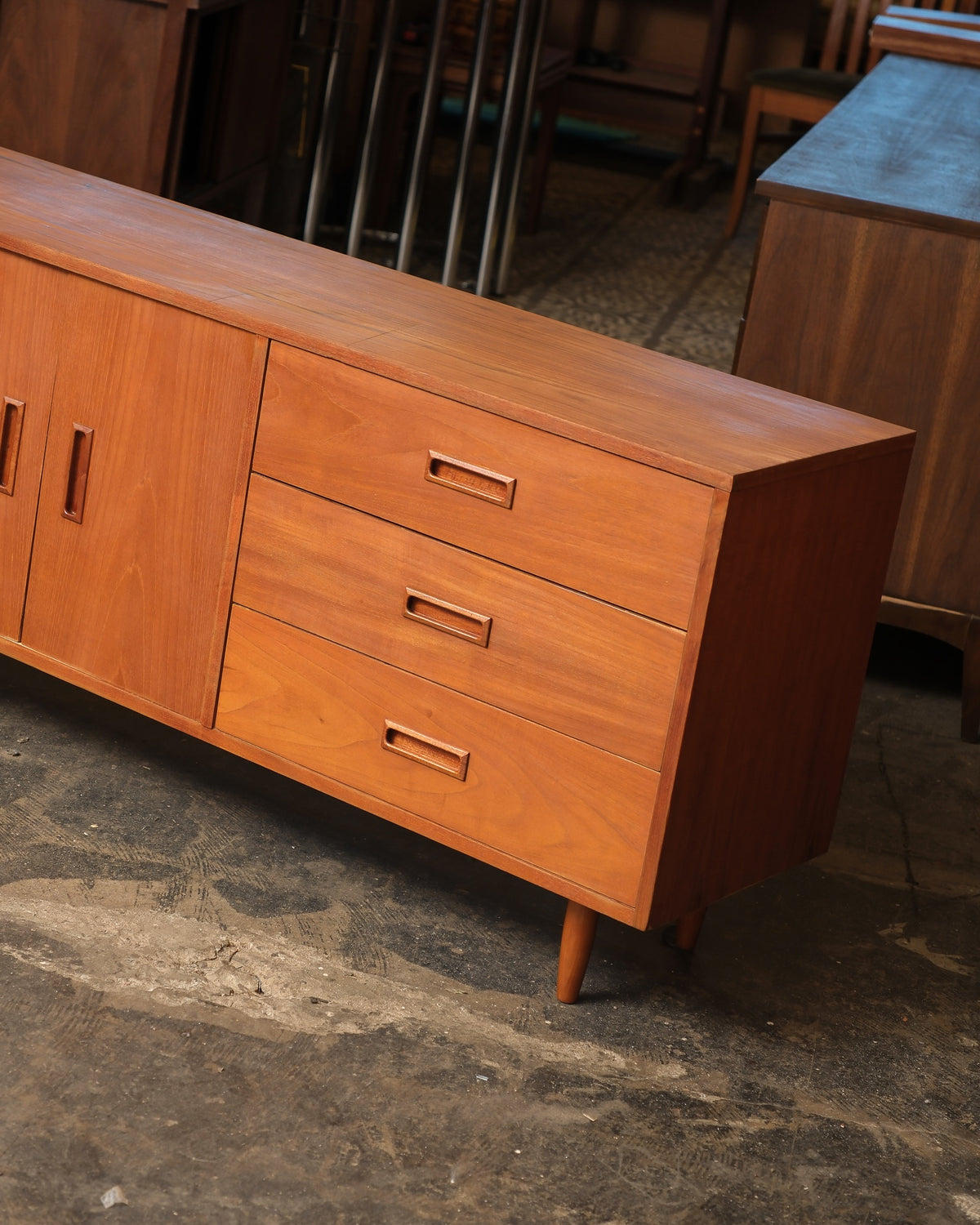 Close-up angled view of the drawer bank and tapered leg on one end of the teak sideboard.