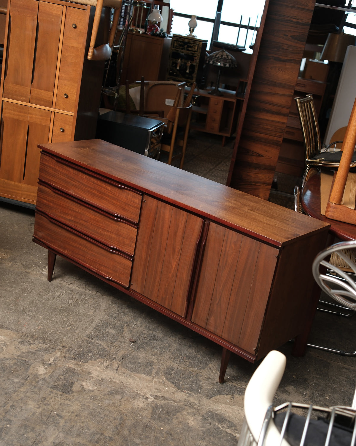 Front angle view of the walnut credenza with three drawers and two paneled cabinet doors closed