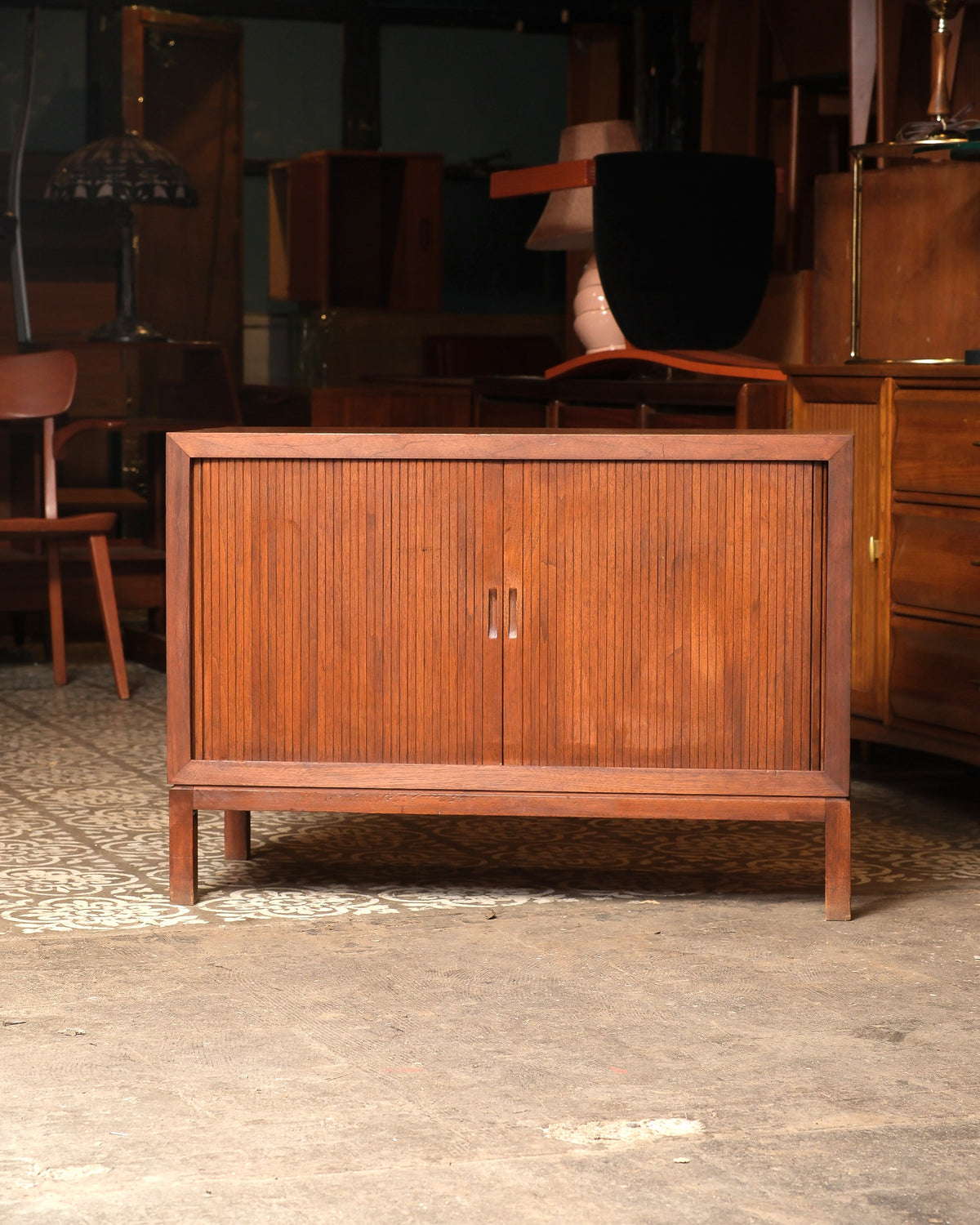 A mid-century modern wooden sideboard cabinet with vertical fluted grain on the doors and straight legs, shown in a furniture showroom.