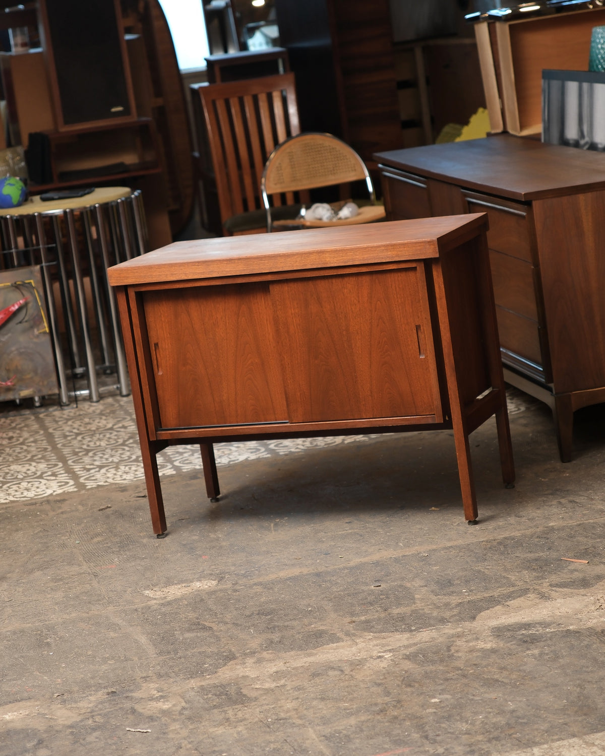 Three-quarter view of the walnut vinyl cabinet showing sliding doors and tapered legs