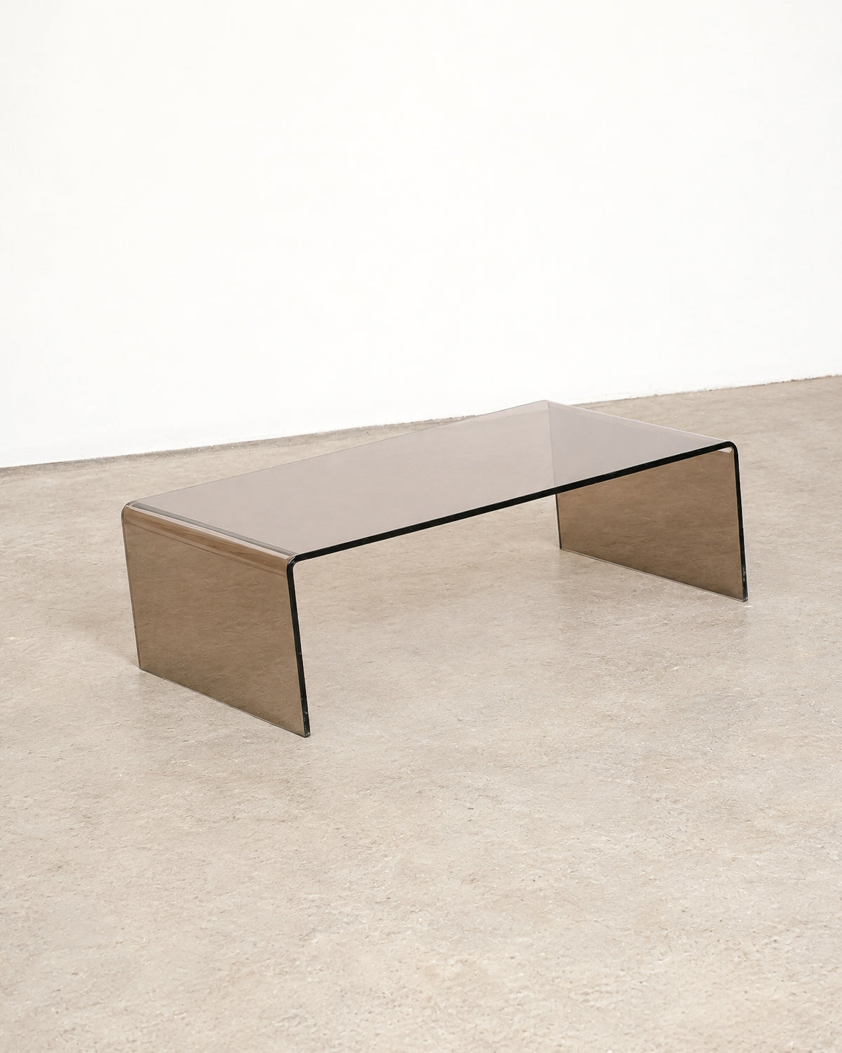 Full side view of the smoked lucite waterfall coffee table against a white wall.
