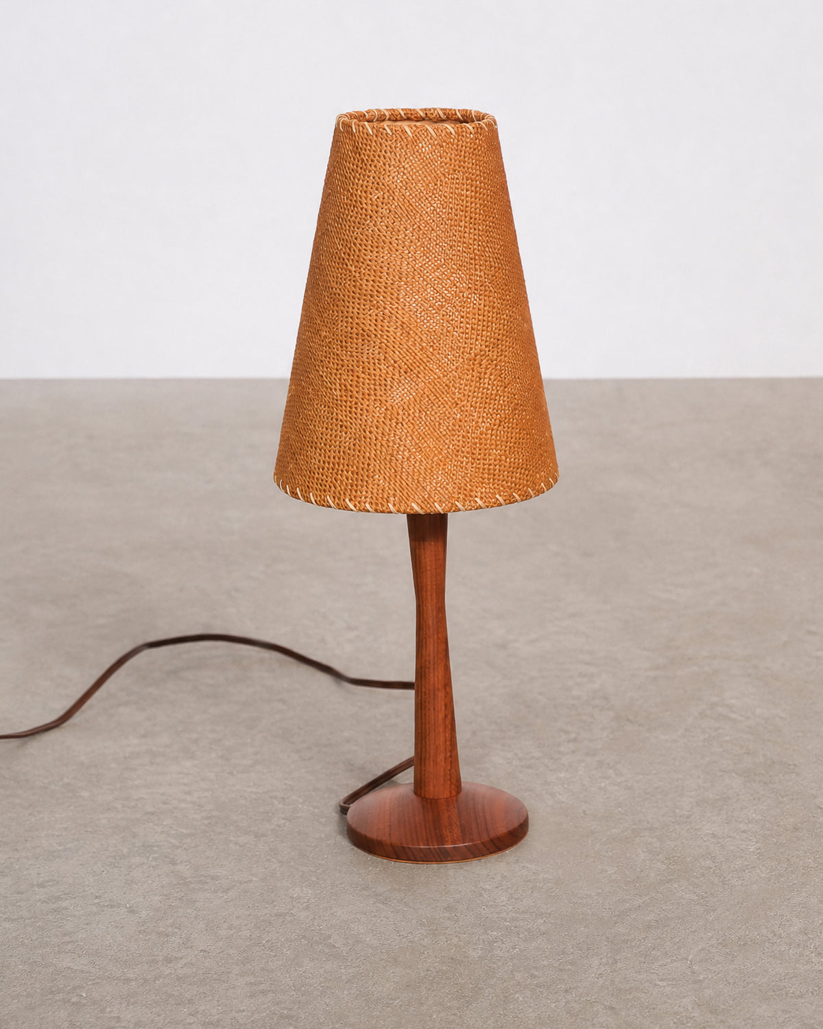 Angled view of the vintage teak table lamp showing the tapered stem, round base, and cone shade.