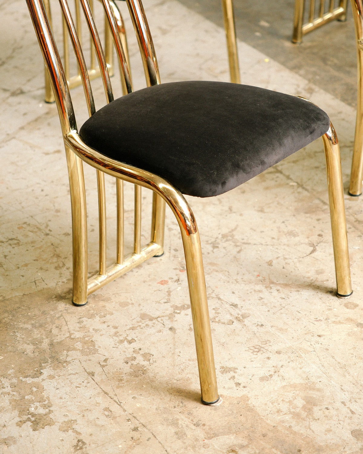 Side view of a brass dining chair showing the black velvet seat and curved leg joinery.