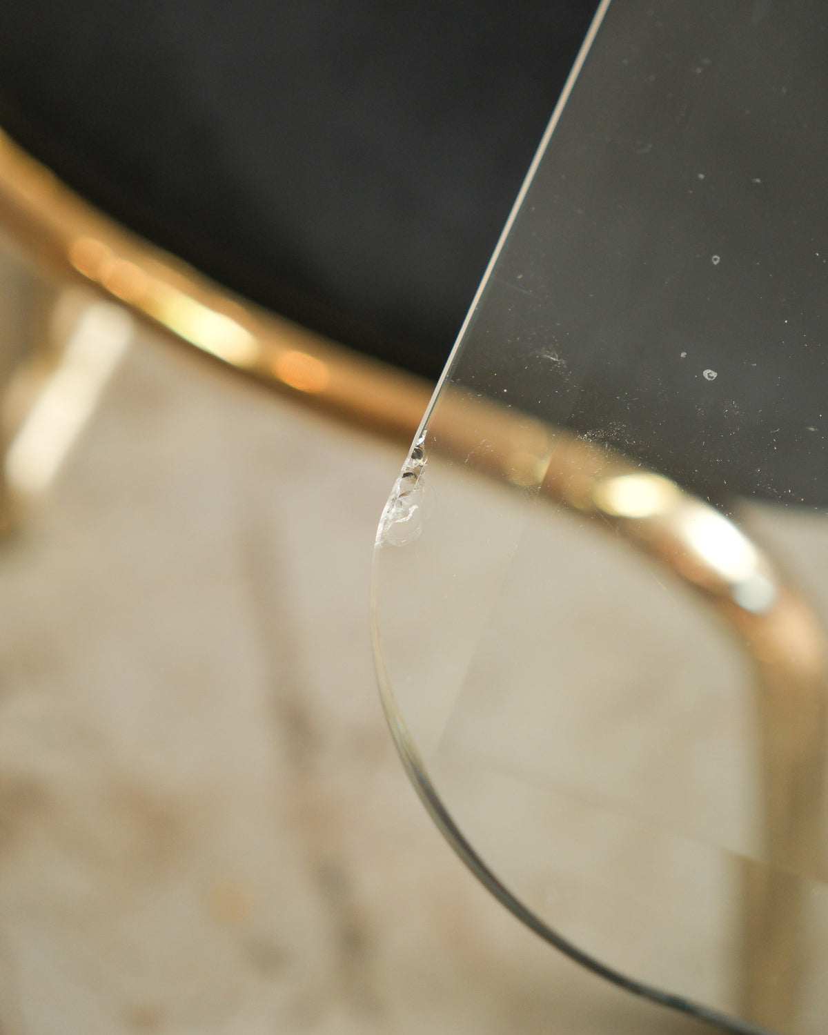 Close-up of a small chip in the glass tabletop edge near the brass chair frame.