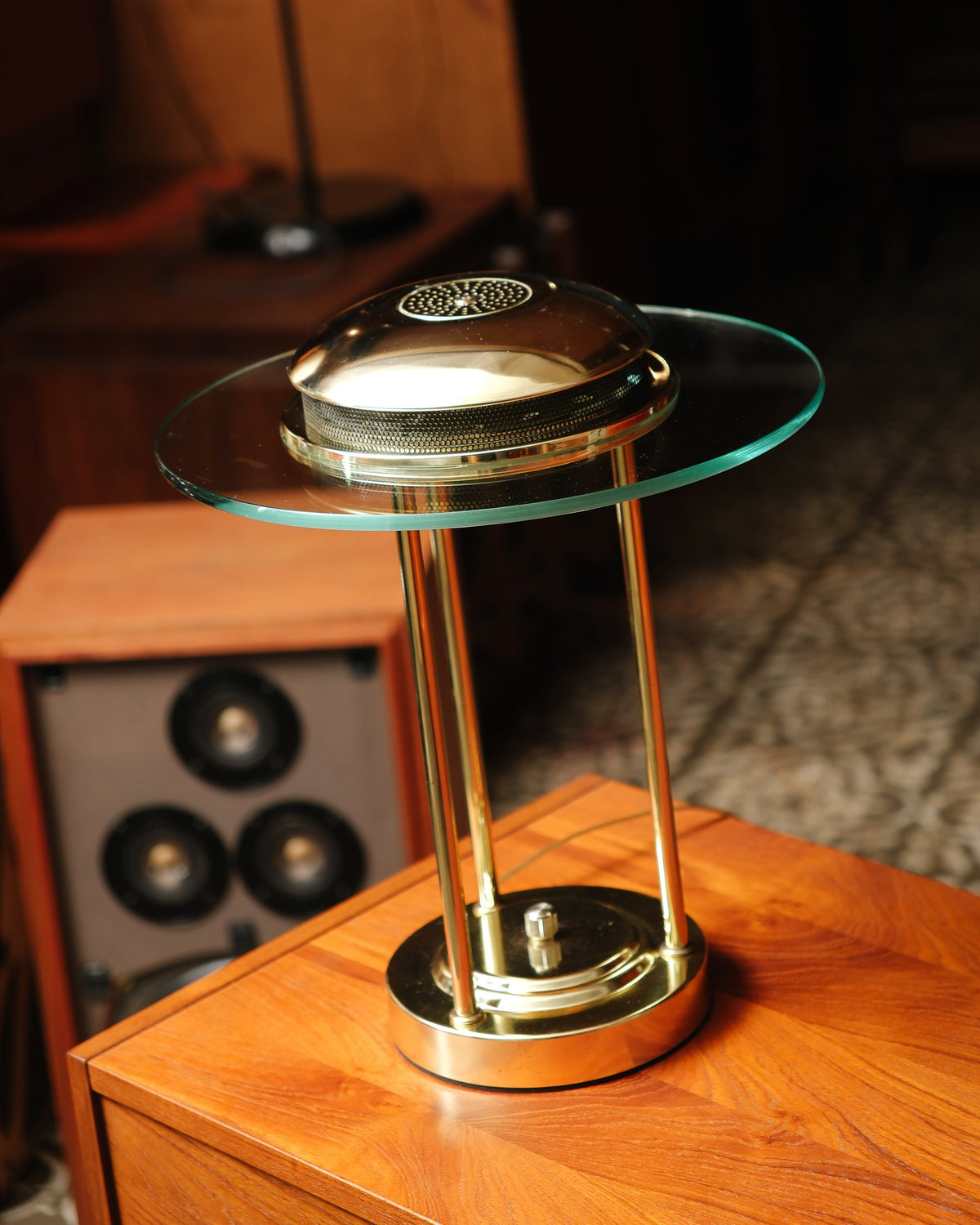 Vintage brass saturn lamp with glass disc shade, shown atop a teak dresser beside a speaker.