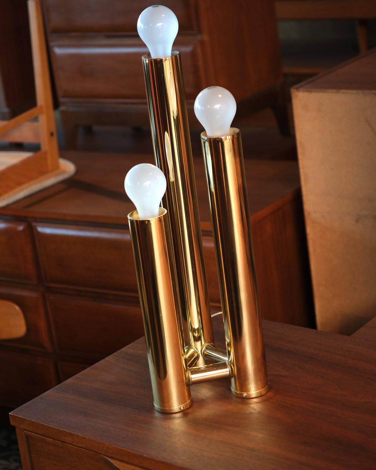 Close-up angle of the brass table lamp showing the three exposed bulbs and polished tubes