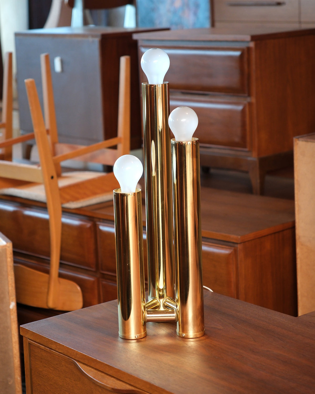 Front view of the brass table lamp on a wooden dresser surrounded by vintage furniture