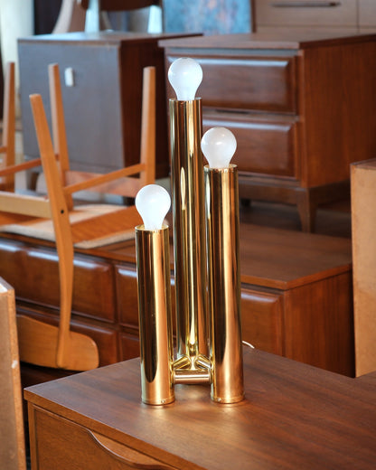 Front view of the brass table lamp on a wooden dresser surrounded by vintage furniture