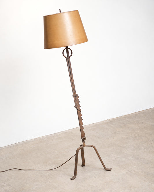Full view of the iron floor lamp with tan shade, angled to show the sculptural tripod base.
