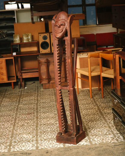 Full view of the carved brutalist media tower standing on a patterned floor amid other vintage furniture pieces.