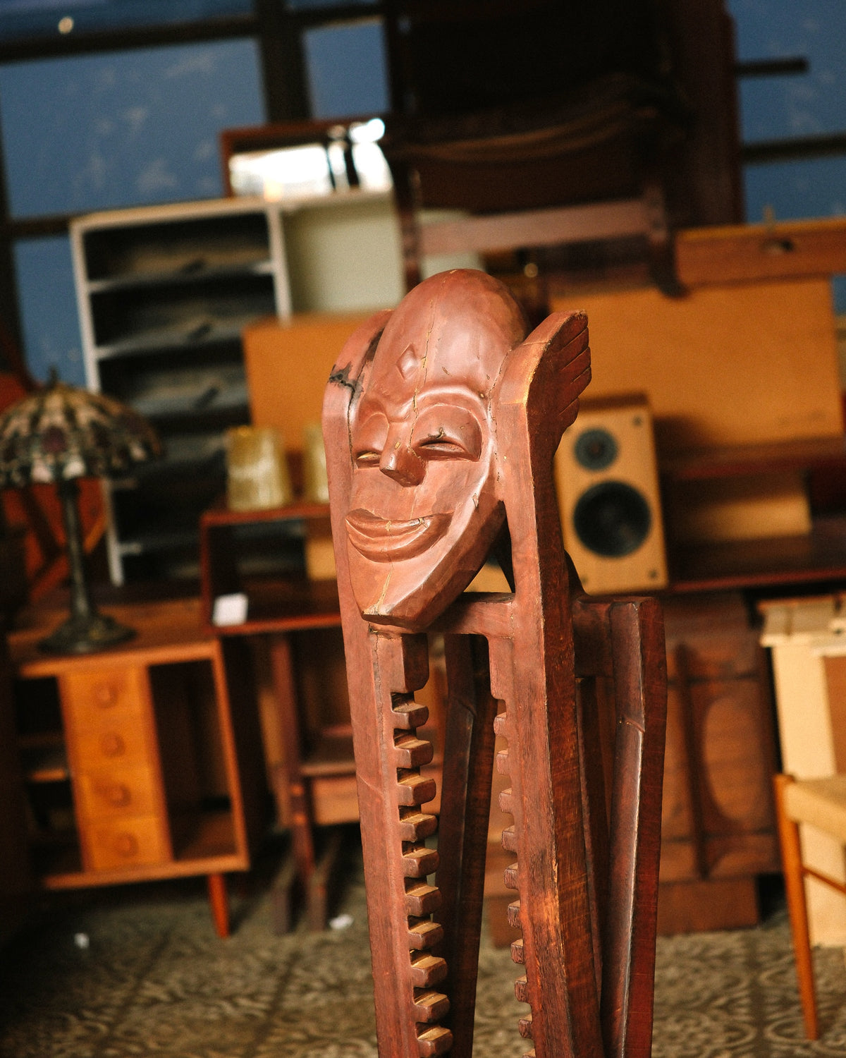 Side angle of the mask face and notched frame, with a Tiffany-style lamp and vintage furniture visible in the background.