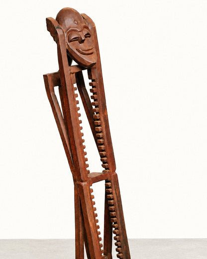 Front view of the tower on a plain background, showing the tall notched legs and carved mask top.
