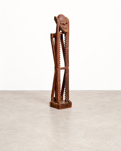 Full straight-on view of the brutalist mask tower against a plain backdrop, showing its full height and square base.