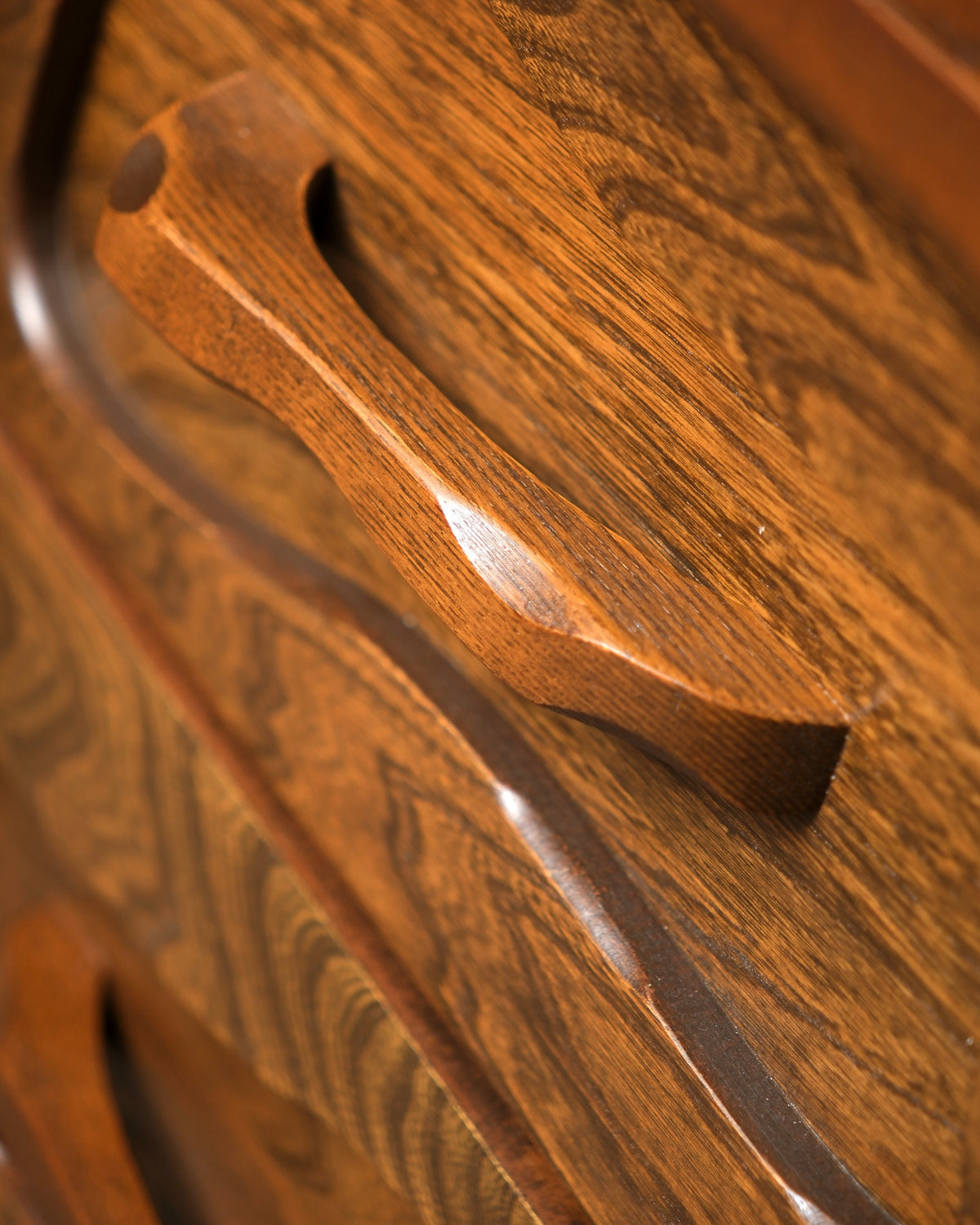 Close-up of a hand-sculpted drawer pull showing the carved wood grain and finish.