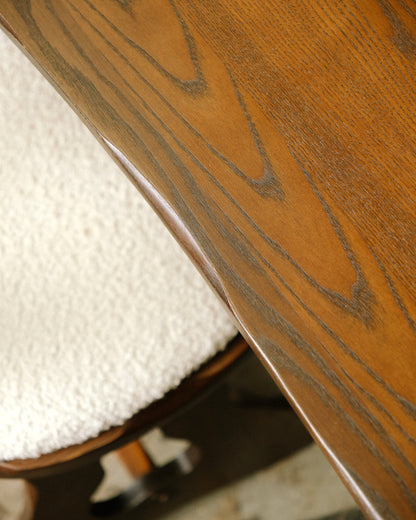 Detail of the oak table edge and grain beside a boucle-upholstered chair seat.
