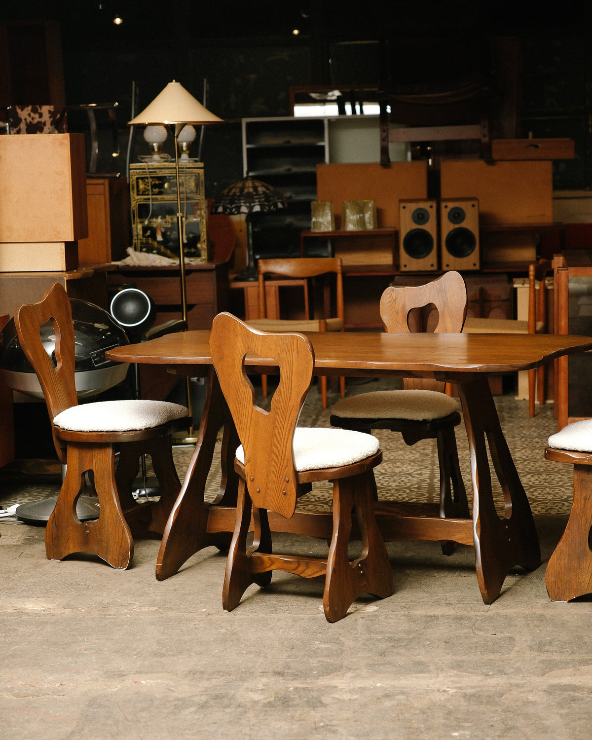 Full view of the brutalist oak dining table with four sculptural chairs in a showroom setting.