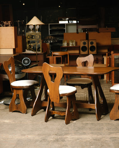 Full view of the brutalist oak dining table with four sculptural chairs in a showroom setting.