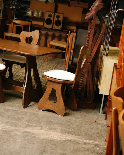 Angled view of the table and chairs among other vintage furniture in the warehouse.