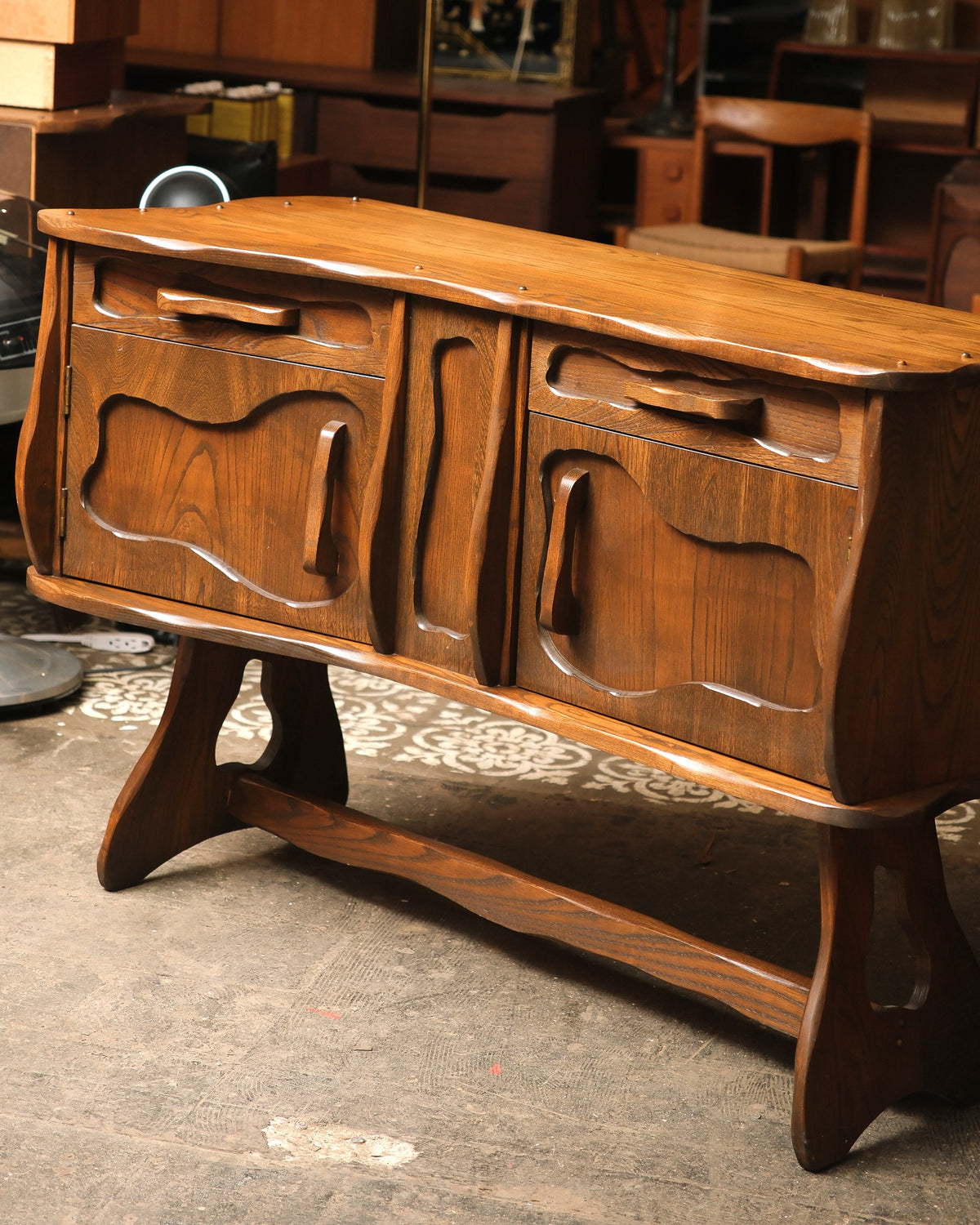 Angled view showing the sideboard's carved doors, drawers, and lower stretcher.