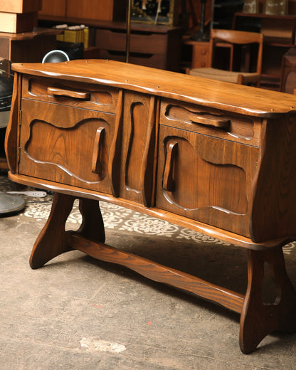Angled view showing the sideboard's carved doors, drawers, and lower stretcher.