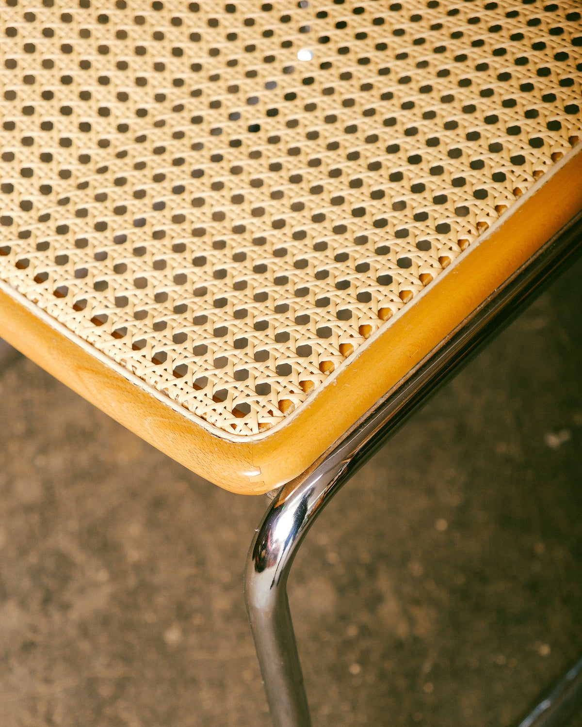 Close-up of the caned seat corner showing the wood trim and chrome leg joint