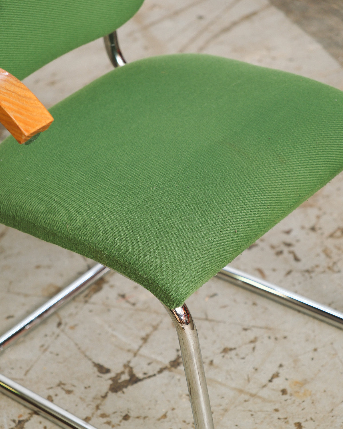 Close-up of the green fabric seat and chrome cantilever leg of the Cesca-style chair.
