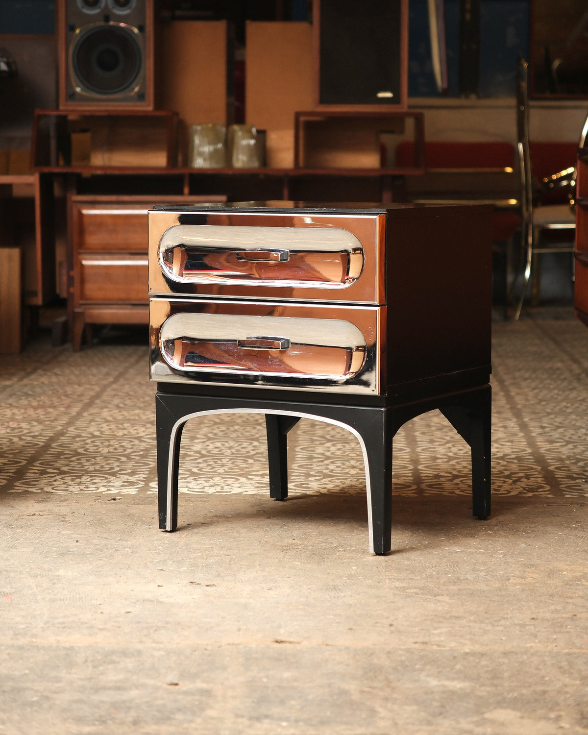 Front view of chrome bedside table showing sculptural drawer pulls and arched legs.