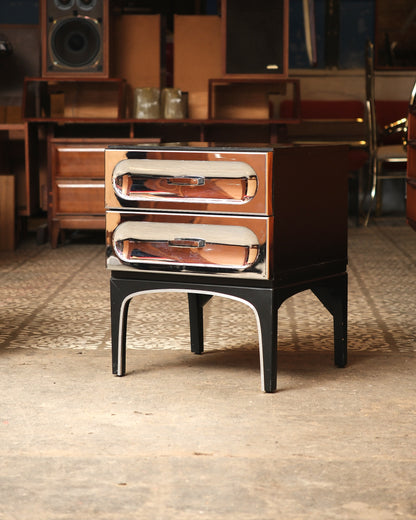 Front view of chrome bedside table showing sculptural drawer pulls and arched legs.