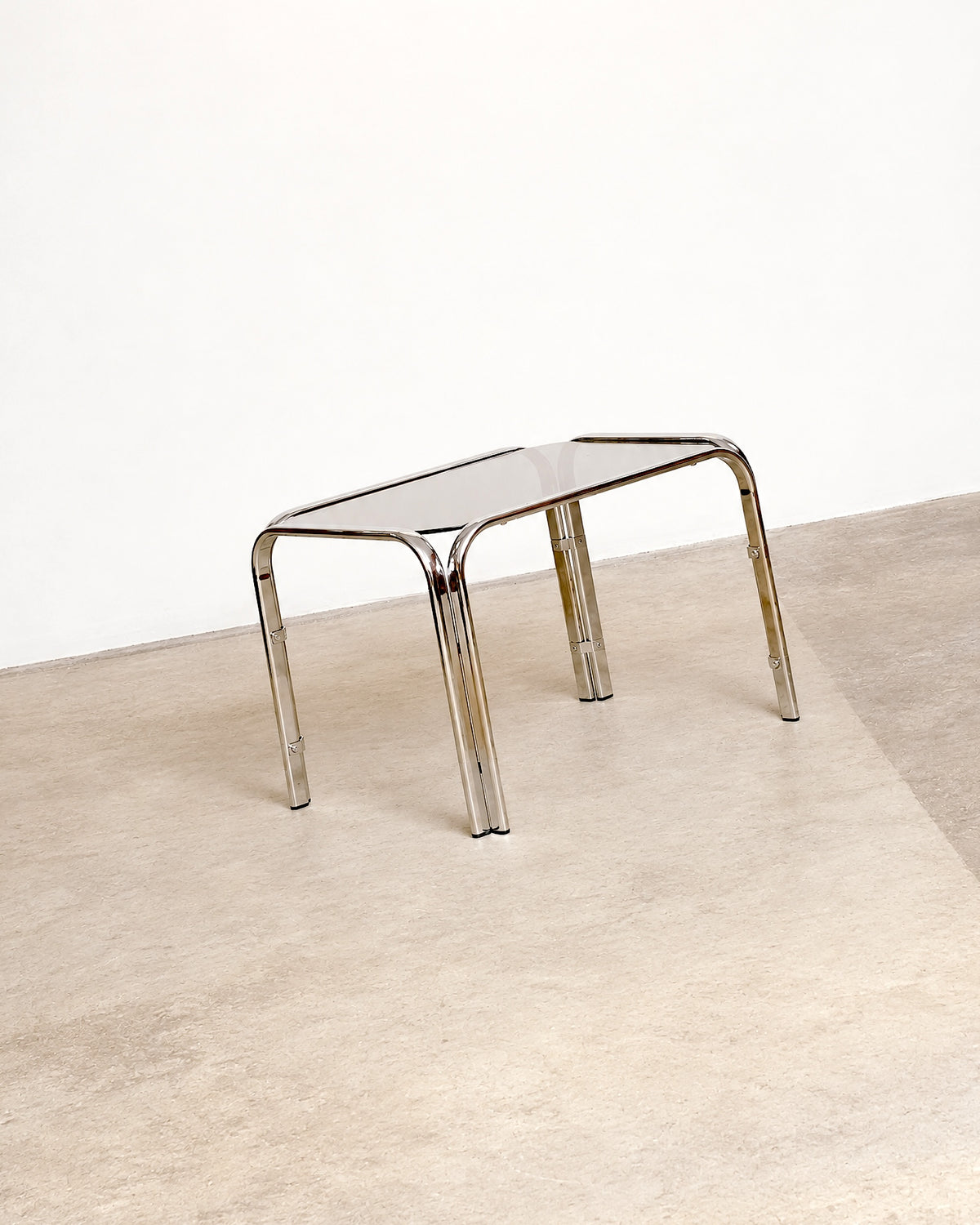 Side angle view of the chrome coffee table showing its splayed leg design and glass top.