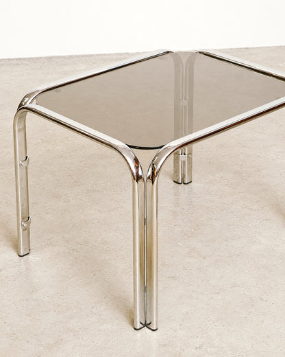 Detail view of the table corner showing the bent chrome frame meeting the smoked glass top.
