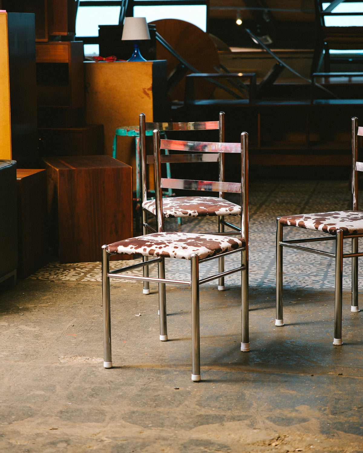Two vintage chrome chairs with cowhide print seats among other vintage furniture in a showroom.