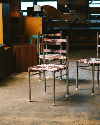 Two vintage chrome chairs with cowhide print seats among other vintage furniture in a showroom.
