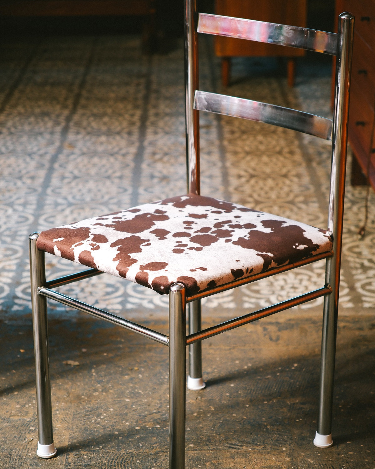 Close angled view of a single chrome chair showing ladder-back frame and cowhide print seat.