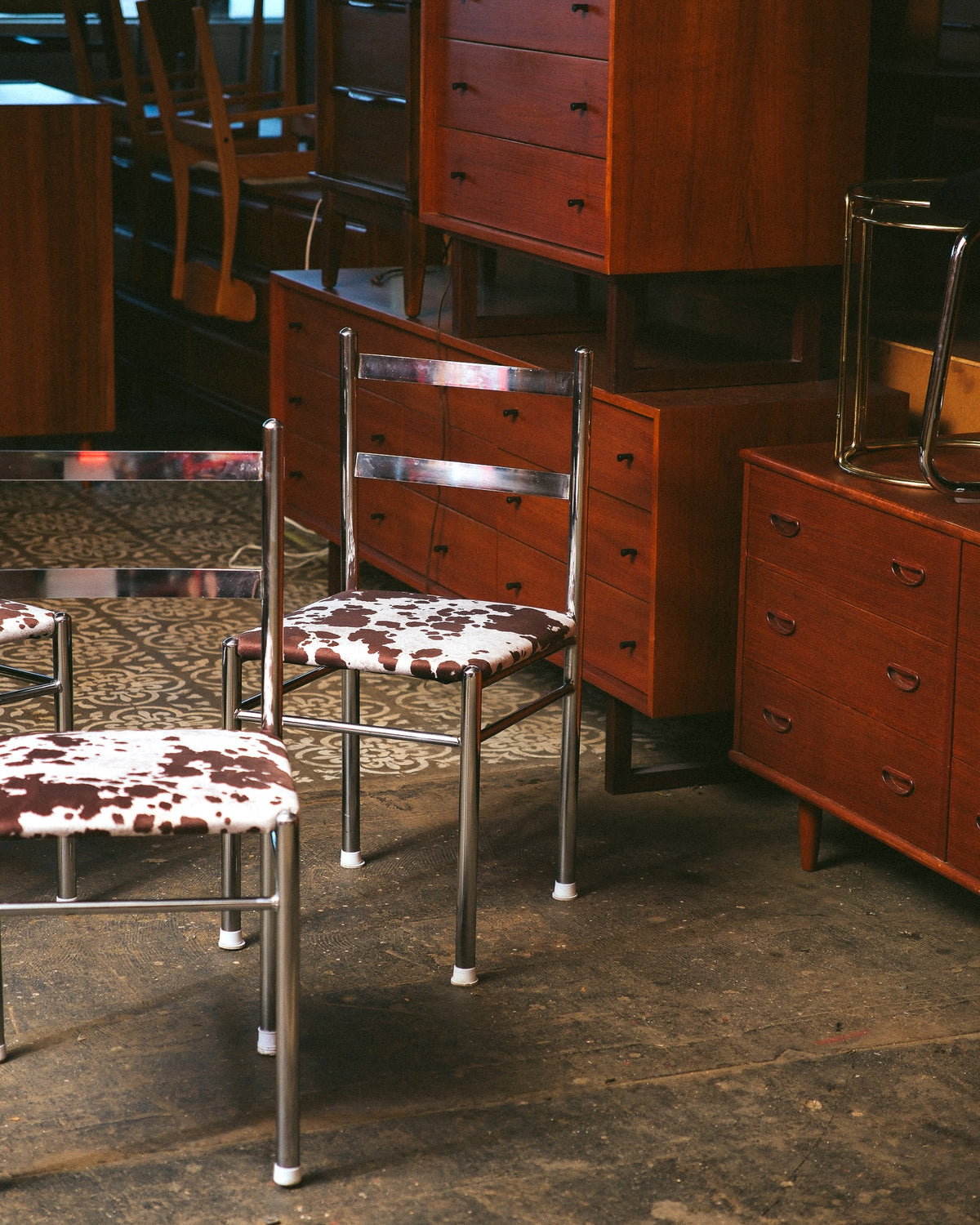 Chrome chair with cowhide seat shown among teak dressers and cabinets in the showroom.