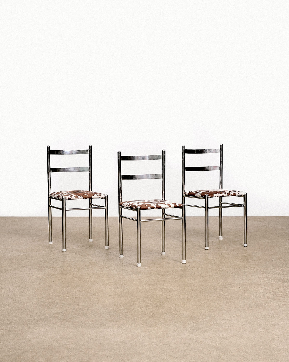 Three chrome chairs with cowhide print seats arranged together against a white backdrop.