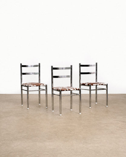 Three chrome chairs with cowhide print seats arranged together against a white backdrop.