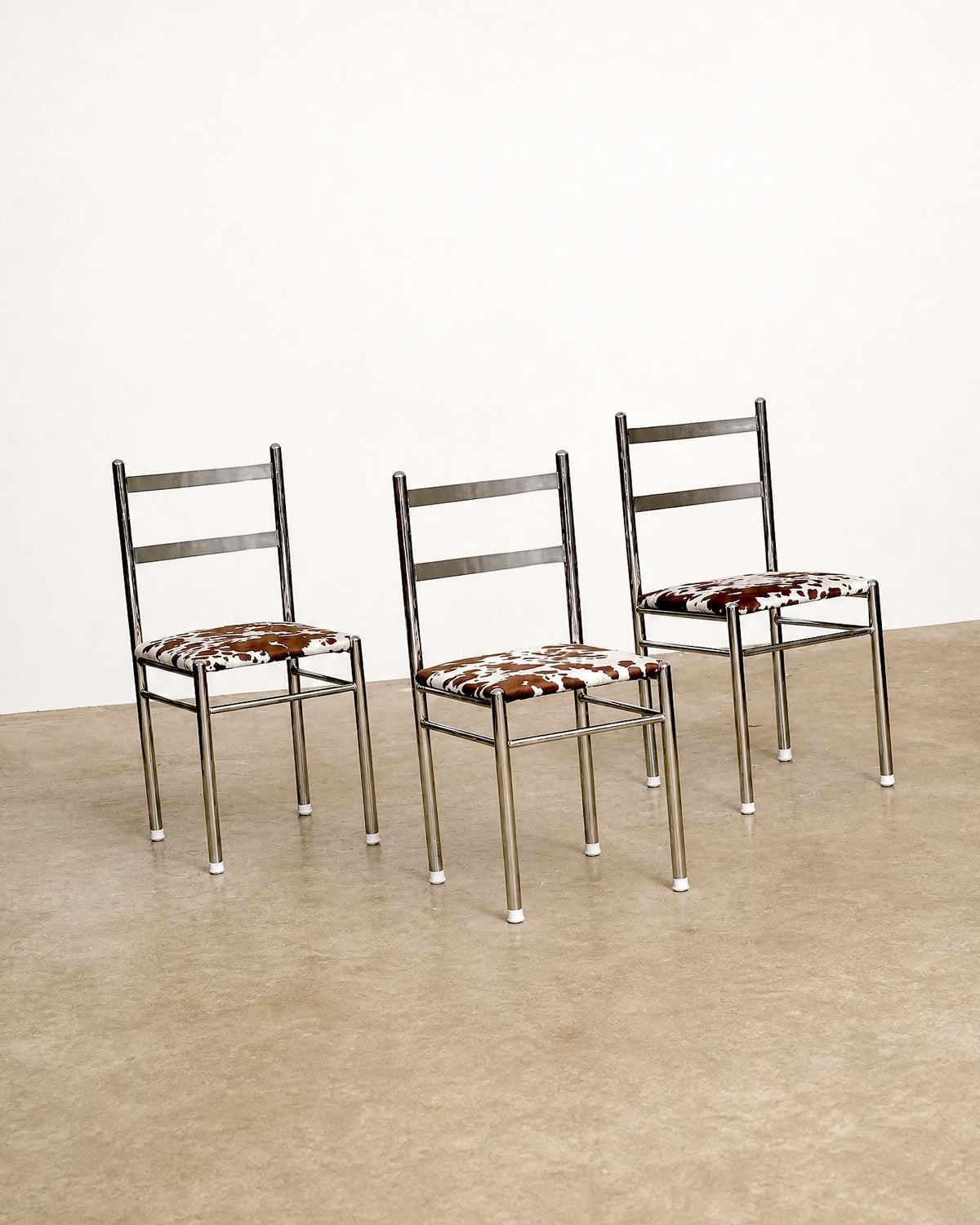 Three chrome chairs with cowhide print seats shown from a wider angle against a white backdrop.