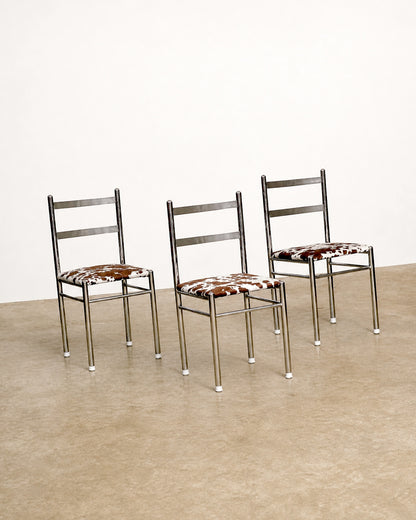 Three chrome chairs with cowhide print seats shown from a wider angle against a white backdrop.