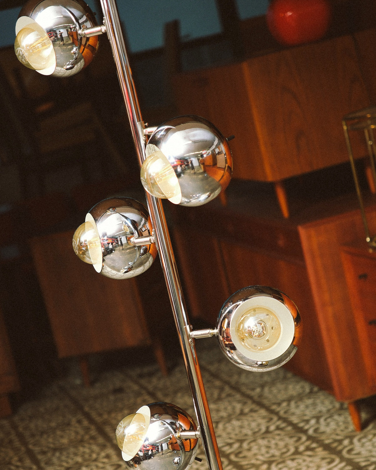 Angled view of the chrome eyeball lamp heads glowing, with a mid-century teak cabinet in the background.