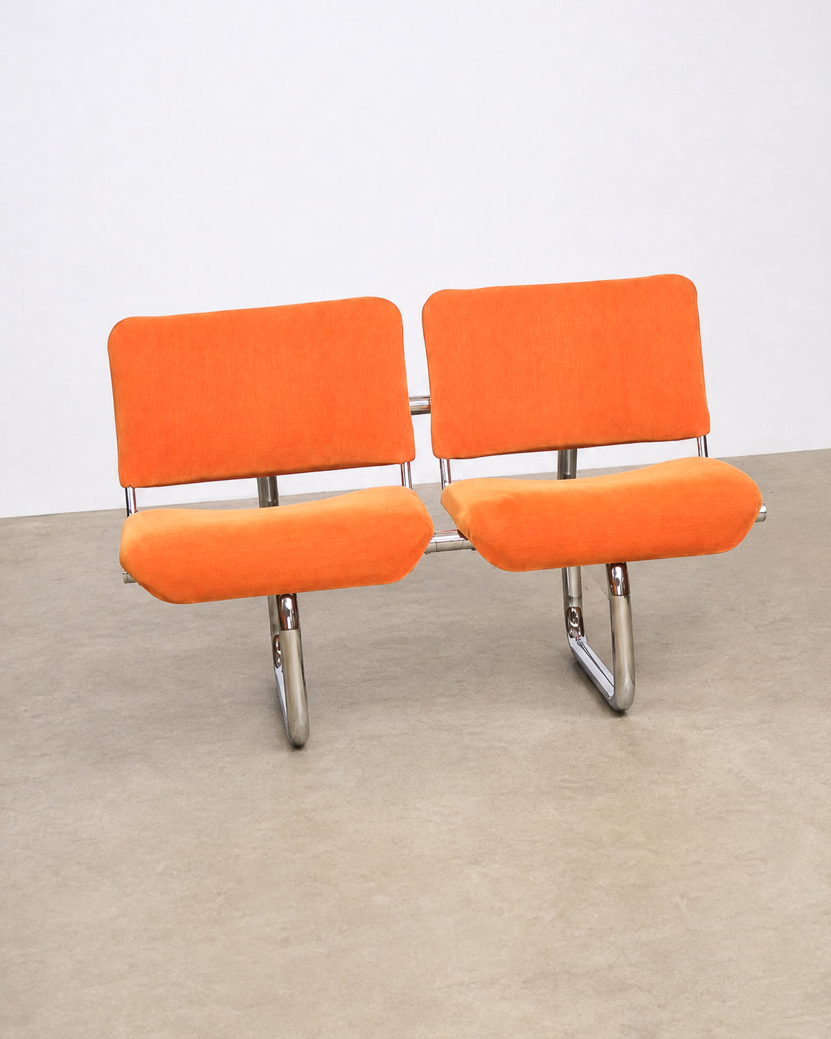 Another angle of the paired orange tubular chairs showing the full chrome frame.
